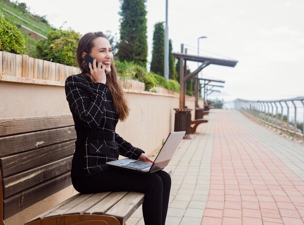 Chica bloguera sonriente está hablando por teléfono inteligente en el parque