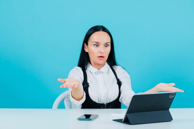 Chica bloguera sorprendida está mirando la pantalla de su tableta con fondo azul