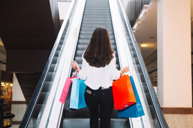 Chica con bolsas en la escalera mecánica