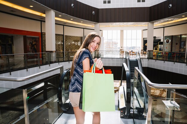 Chica con bolsas de papel haciendo gestos en el centro comercial