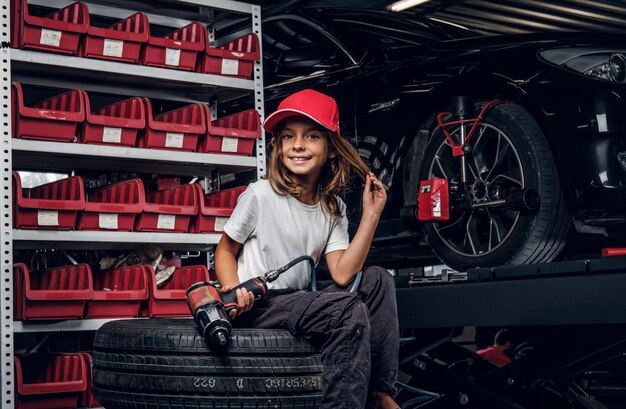 Una chica bonita posa para el fotógrafo mientras se sienta en un servicio de autos oscuro con un taladro neumático.