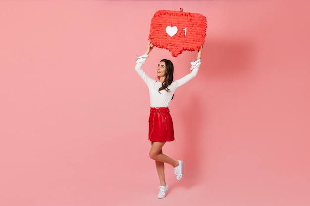 Chica bronceada en falda de cuero de moda rebota sobre fondo rosa con decoración en forma de como de Instragram.