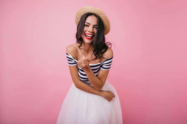 Chica bronceada sensual con maquillaje brillante riendo. Retrato interior de mujer increíble en falda blanca.