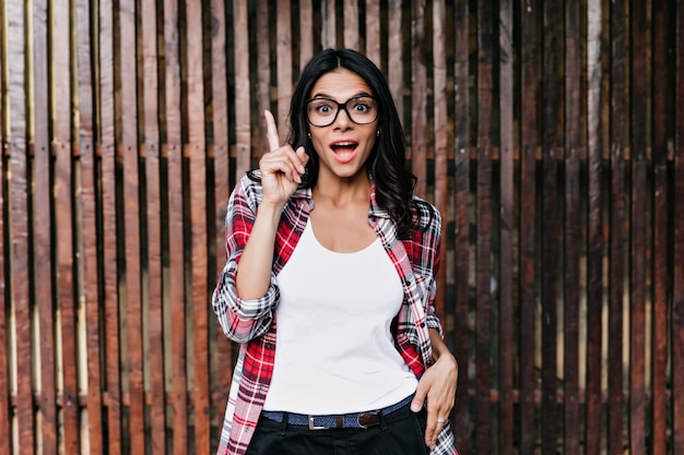 La chica de buen humor tiene una buena idea. Foto al aire libre de dama latina emocional aislada en la pared de madera.