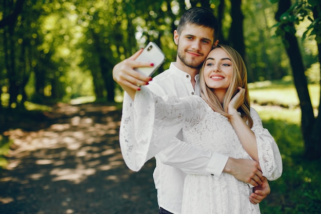 chica con cabello claro y un vestido blanco está tomando una foto en un bosque soleado con su novio
