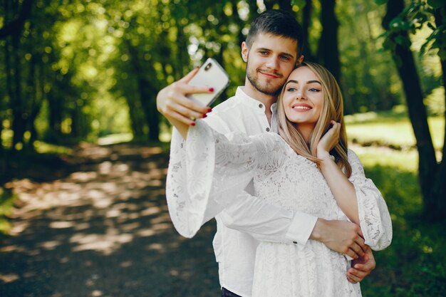 chica con cabello claro y un vestido blanco está tomando una foto en un bosque soleado con su novio