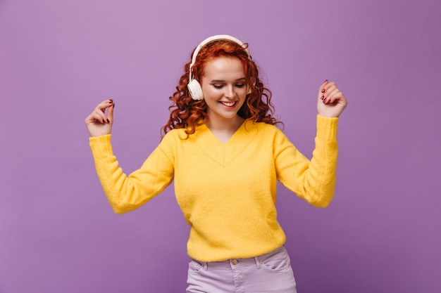 Chica con cabello ondulado baila en auriculares en la pared lila