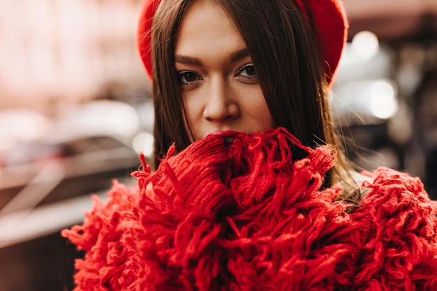 Una chica de cabello oscuro y ojos marrones se cubre la cara con las manos Imagen de una mujer con abrigo rojo y sombrero