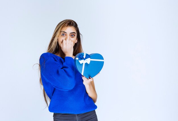 La chica con una caja de regalo azul parece confundida y sorprendida.