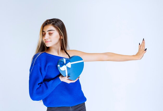 Chica con una caja de regalo con forma de corazón azul parando a otros.