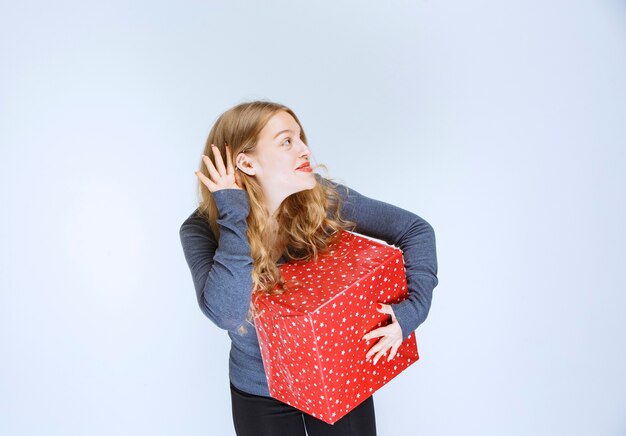 Chica con una caja de regalo roja abriendo la oreja y escuchando atentamente.