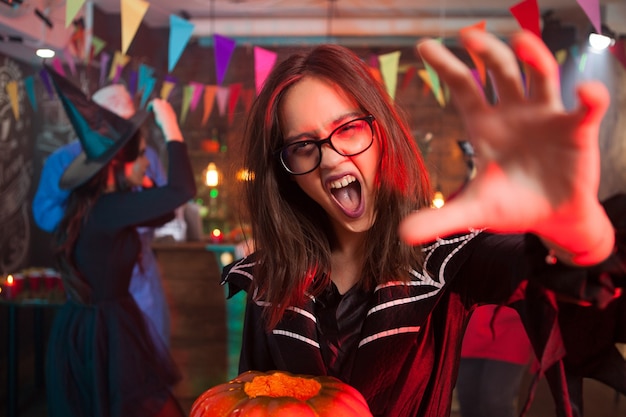 Chica con una calabaza para halloween gritando y alcanzando la cámara. Retrato de una hermosa niña en la fiesta de halloween de cerca.