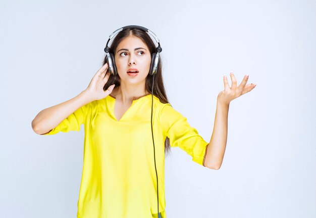 Chica de camisa amarilla con auriculares y mirando confundida y aterrorizada.