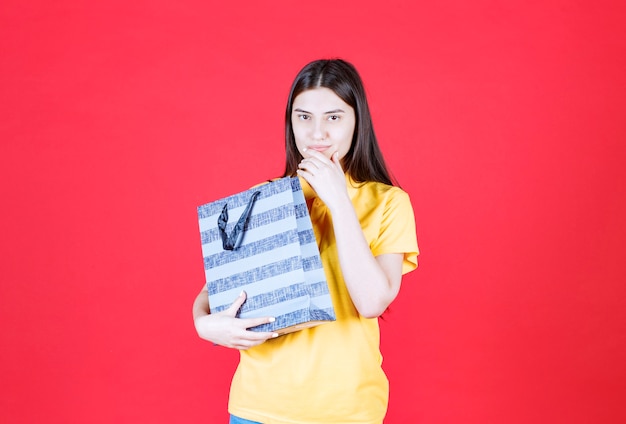 Chica con camisa amarilla sosteniendo una bolsa azul y pensando o teniendo una buena idea.