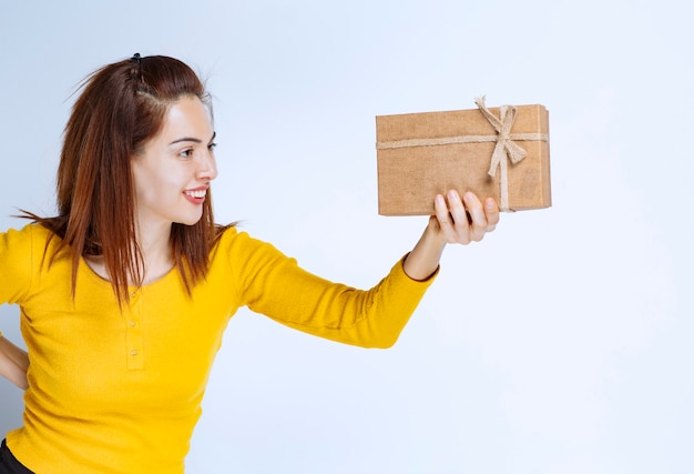 Chica de camisa amarilla sosteniendo una caja de regalo de cartón.