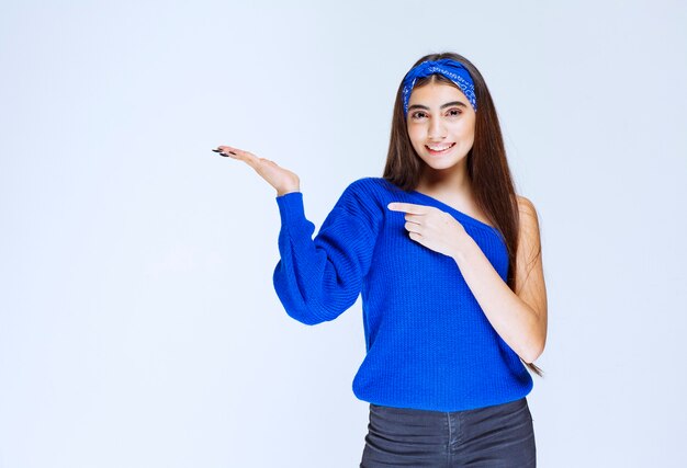 Chica con camisa azul apuntando hacia el lado izquierdo.