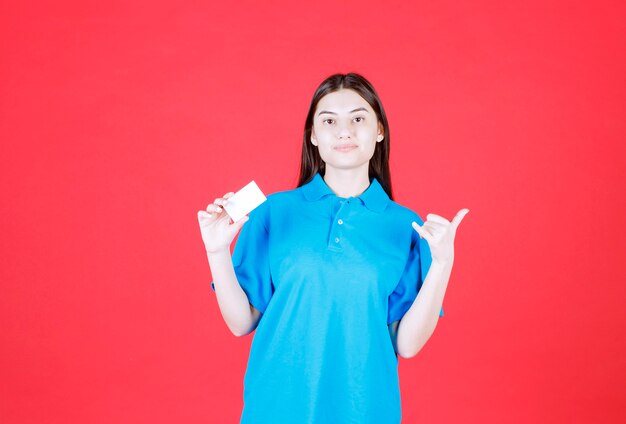 Chica con camisa azul presentando su tarjeta de visita y apuntando a su colega alrededor