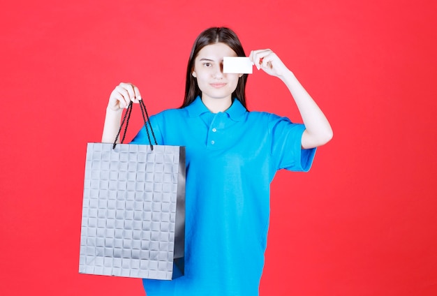 Chica con camisa azul sosteniendo una bolsa de compras púrpura y presentando su tarjeta de visita