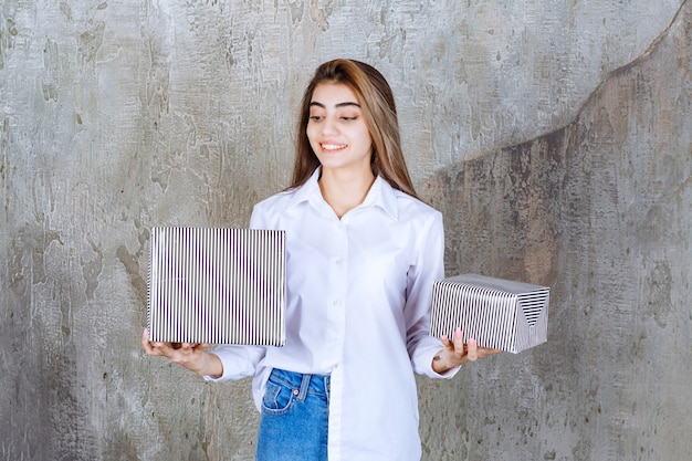 Chica con camisa blanca con cajas de regalo plateadas.