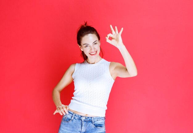 Chica en camisa blanca haciendo señal de mano de disfrute.