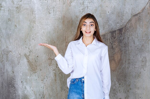 Chica con camisa blanca de pie sobre un muro de hormigón y notando a la persona alrededor.