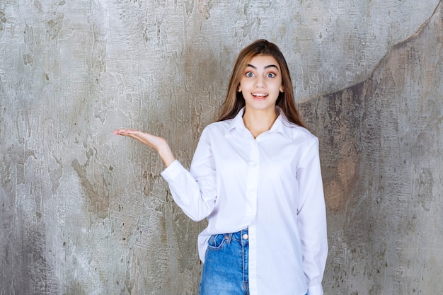 Chica con camisa blanca de pie sobre un muro de hormigón y notando a la persona alrededor.