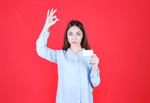 Chica con camisa blanca presentando su tarjeta de visita y mostrando un signo de mano positivo.