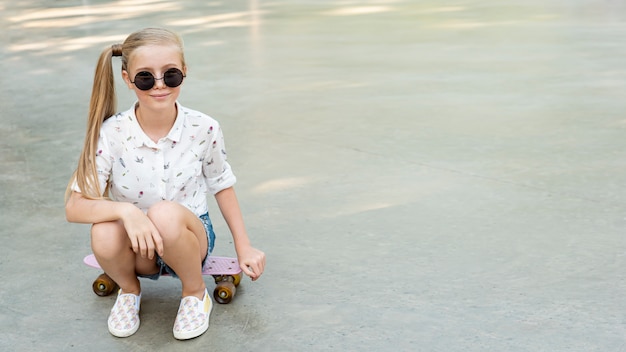 Chica con camisa blanca sentada en patineta