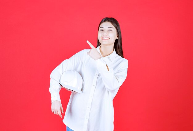 Chica con camisa blanca sosteniendo un casco blanco y apuntando a algún lugar