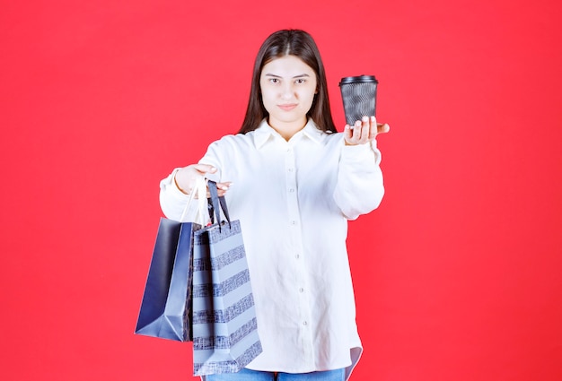 Chica con camisa blanca sosteniendo varias bolsas de la compra y compartiendo con una taza de café para llevar negra