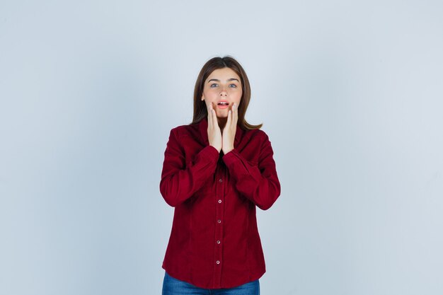 chica en camisa burdeos cogidos de la mano cerca de la boca y mirando sorprendido.