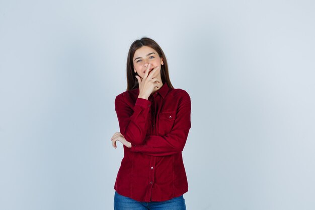 chica en camisa burdeos sosteniendo la mano en la boca y mirando alegre.