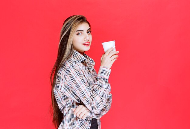 Chica en camisa de cuadros sosteniendo una taza de café desechable blanca