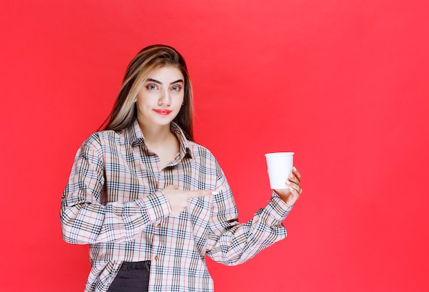 Chica en camisa de cuadros sosteniendo una taza de café desechable blanca