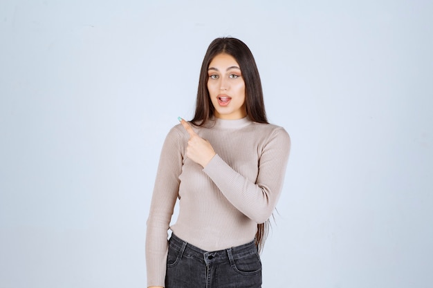 Chica con camisa gris apuntando a algo a la izquierda.