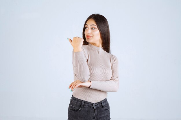 Chica con camisa gris apuntando a algo a la izquierda.