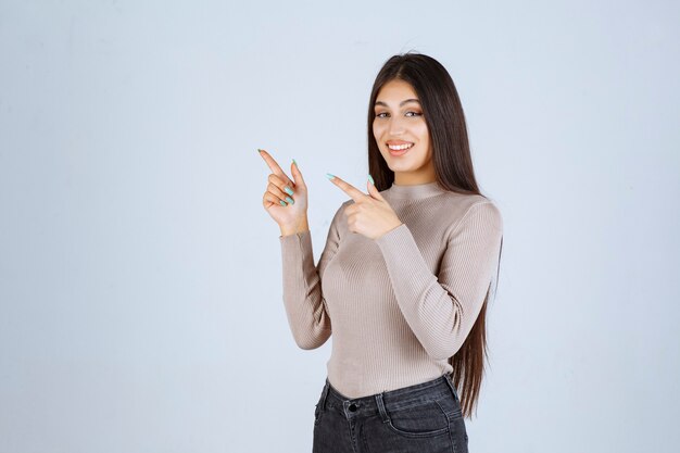 Chica con camisa gris apuntando a algo.