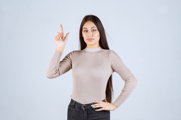 Chica con camisa gris apuntando a algo.