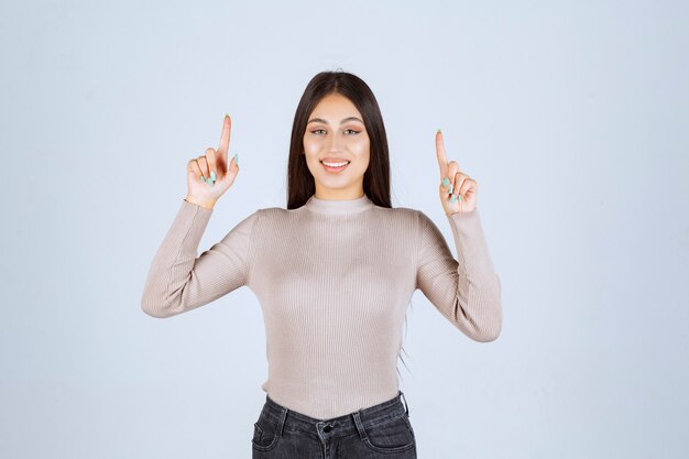 Chica con camisa gris apuntando a algo.