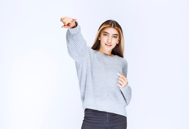 Chica de la camisa gris apuntando a algún lugar o alguien.