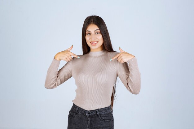 Chica de camisa gris apuntando a sí misma.