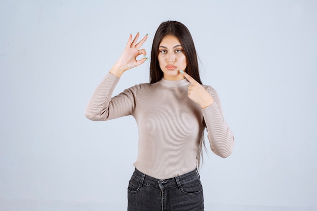 Chica con camisa gris apuntando a su boca.