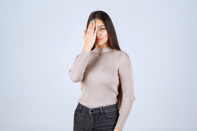 Chica en camisa gris cubriendo e higind su rostro.