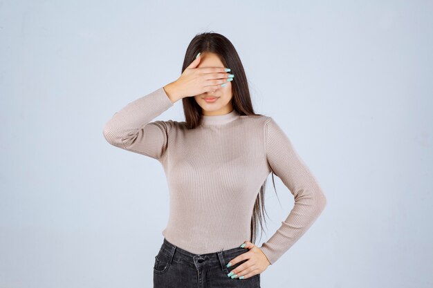 Chica en camisa gris cubriendo e higind su rostro.