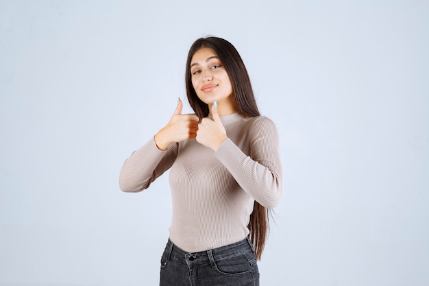 Chica en camisa gris haciendo pulgar arriba signo.