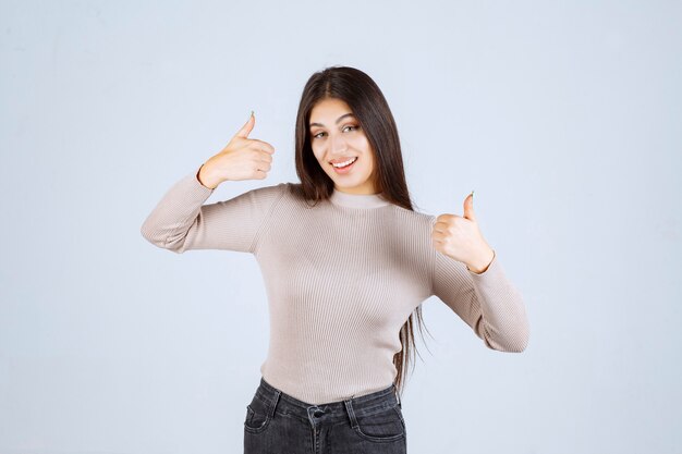 Chica en camisa gris haciendo pulgar arriba signo.