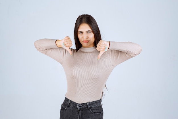 Chica en camisa gris haciendo señal con el pulgar hacia abajo.