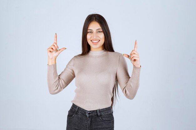 Chica en camisa gris mostrando algo arriba y emocionándose.