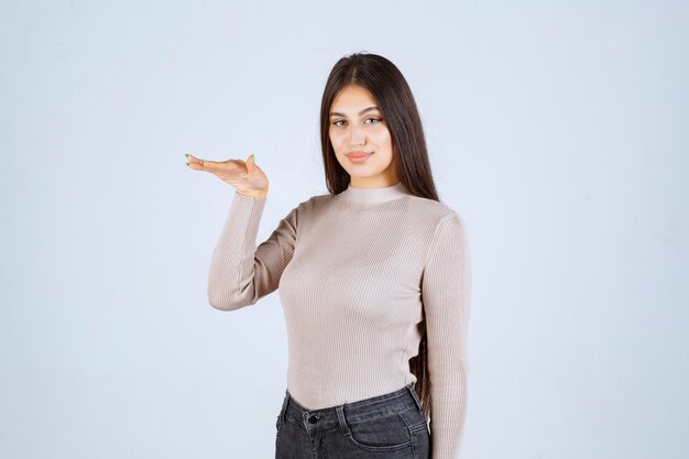 Chica con camisa gris mostrando algo en la mano.