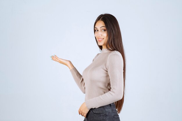 Chica con camisa gris mostrando algo en la mano.